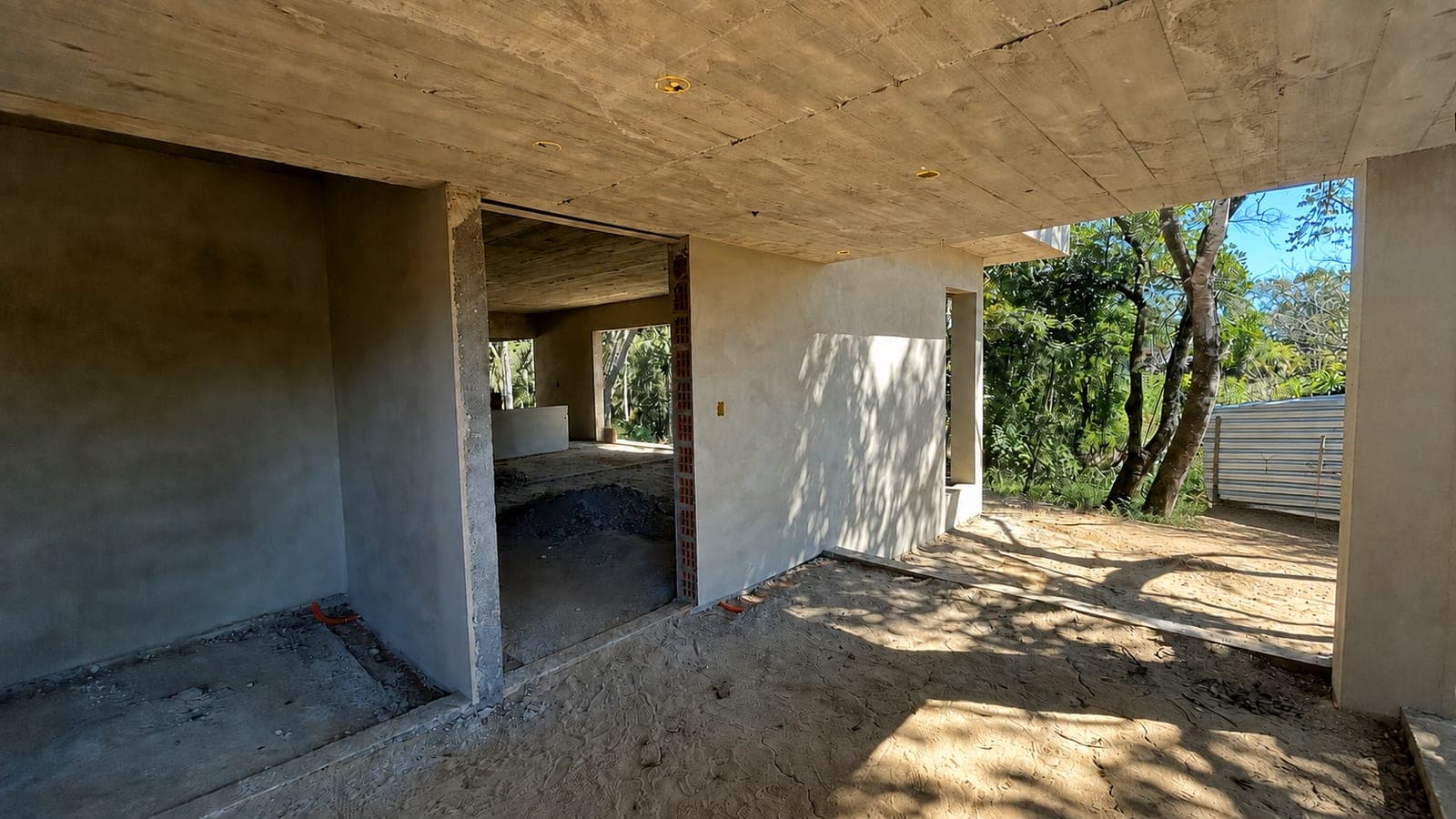 Entrada da sala em obra, coberta por laje de concreto aparente, com o vão da porta principal e a sala visível ao fundo