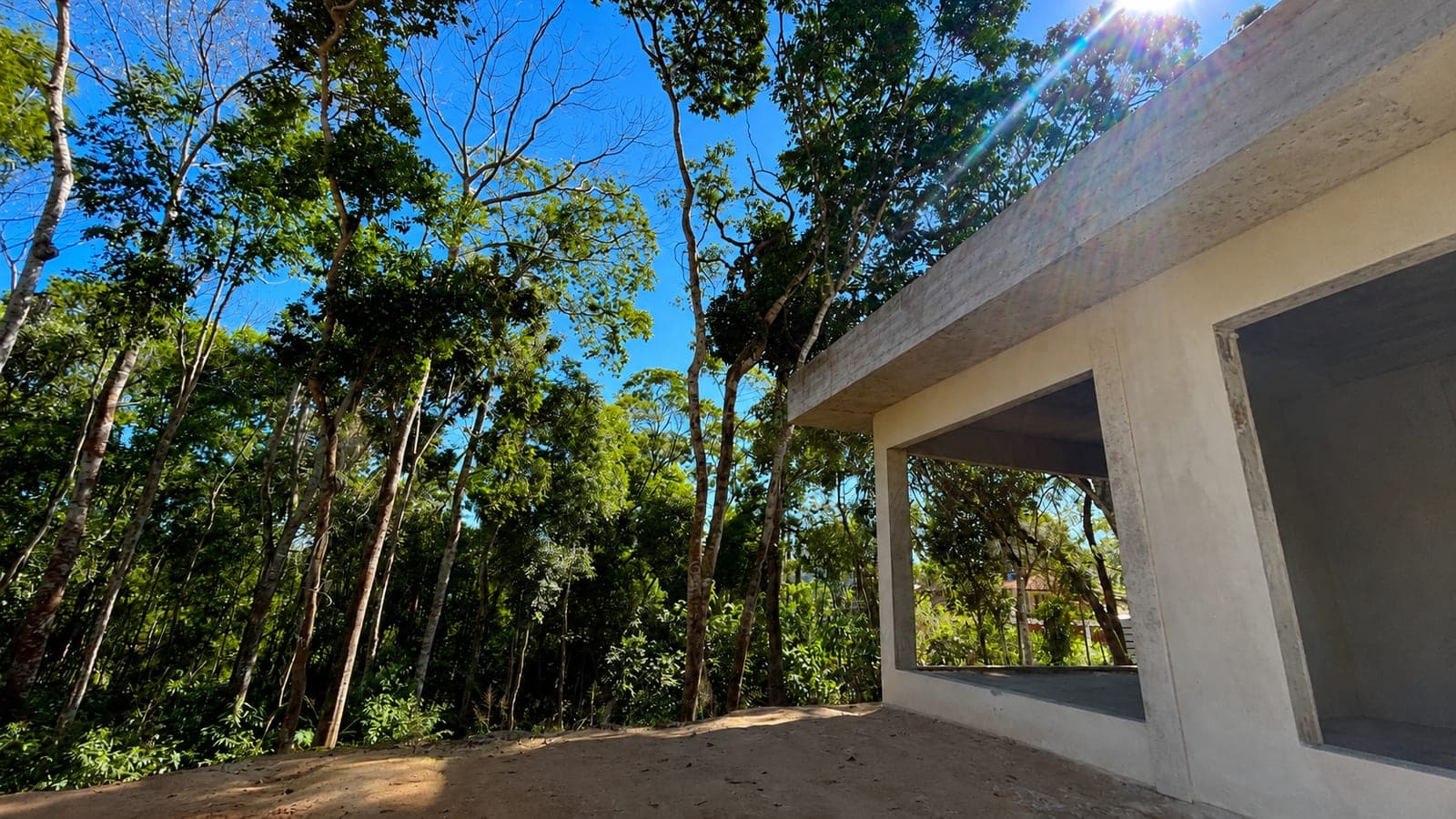 Varanda em obra, coberta por laje de concreto aparente, com grandes vãos abertos para a mata no caminho até a piscina