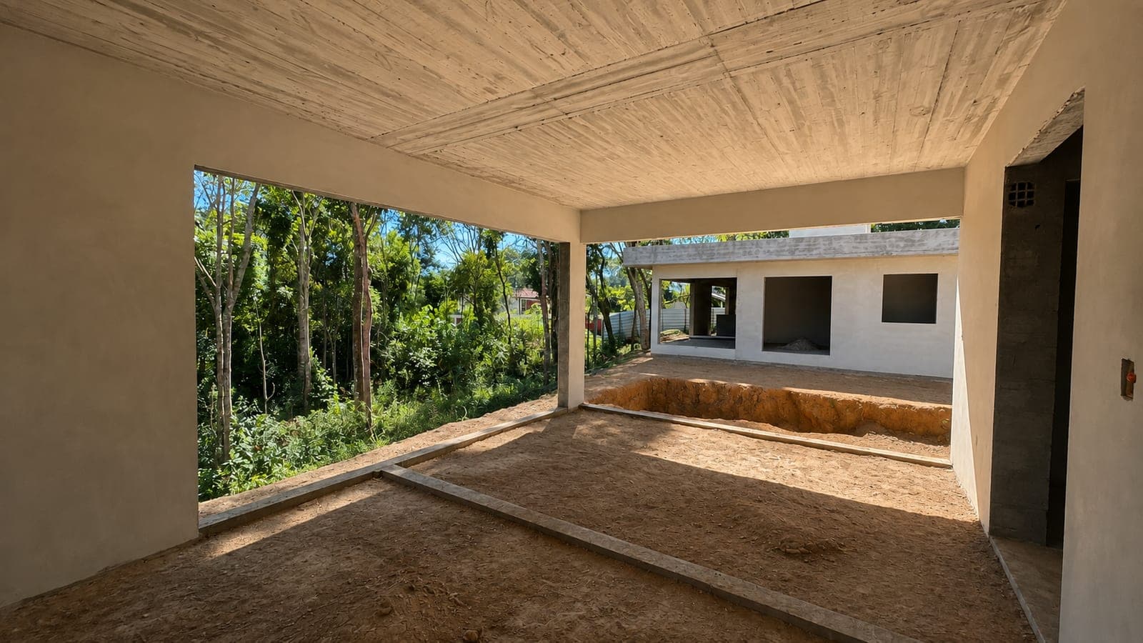 Área gourmet em obra, com laje de concreto aparente, grande vão aberto para a mata e a escavação da piscina à frente, com a casa principal ao fundo