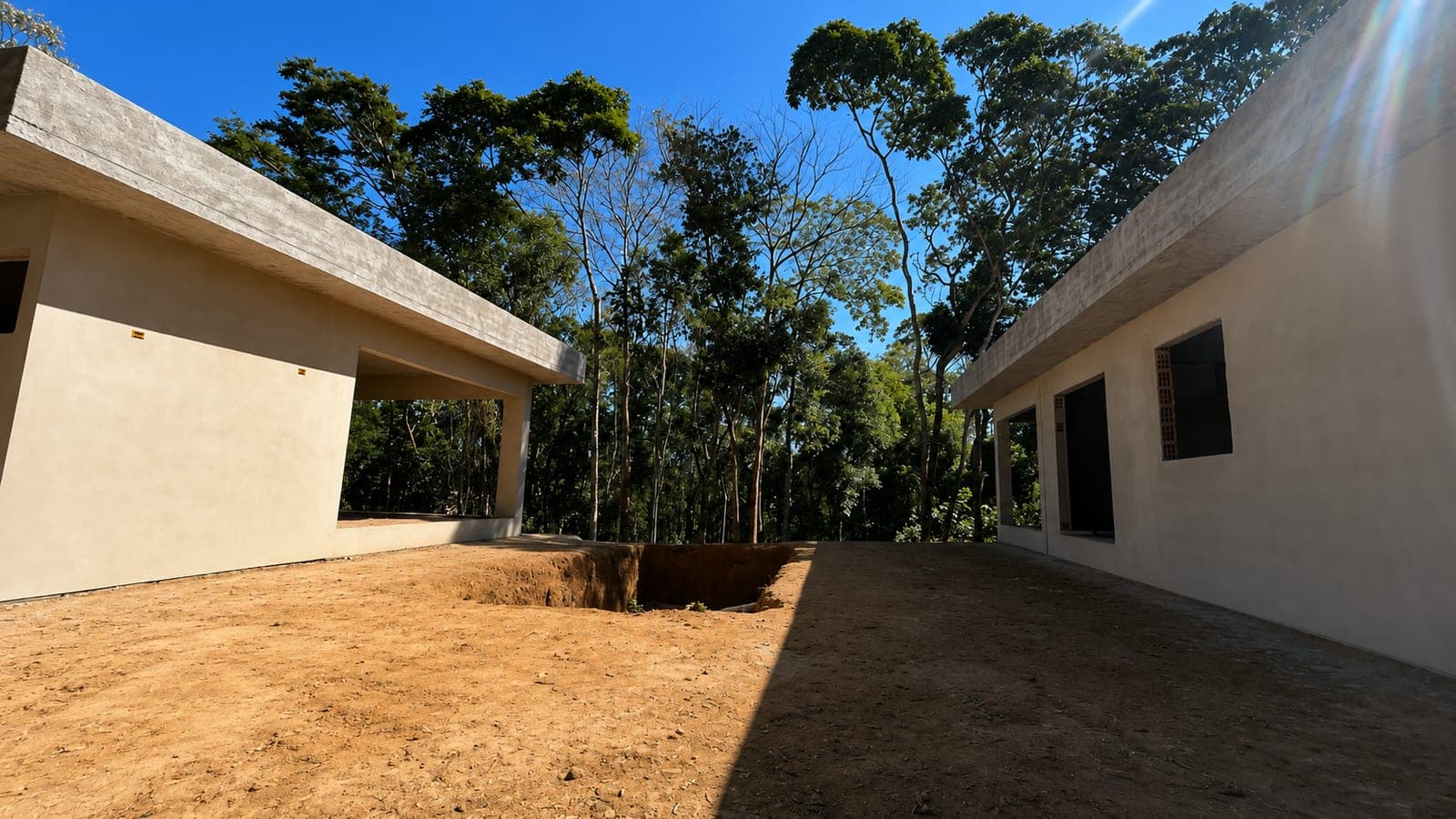 Área da piscina em obra, entre a casa principal e a área gourmet, com a escavação aberta no terreno e a mata ao fundo